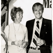 A smiling woman and a man in a shirt and striped tie holding drinks at an event.